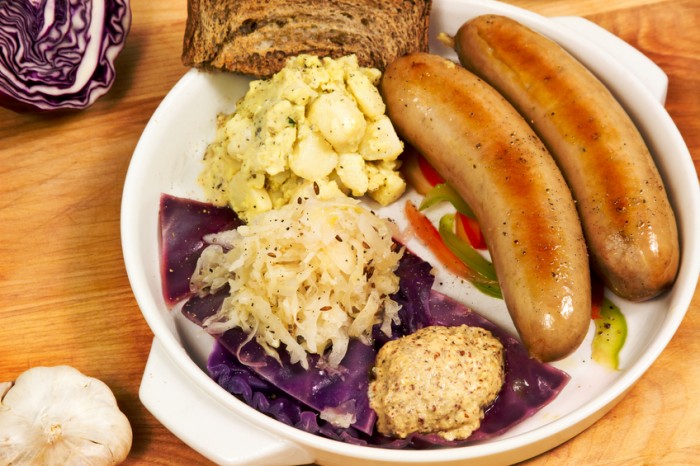 "Traditional German meal with bratwurst, sauerkraut, cabbage, potato salad, mustard and rye bread."