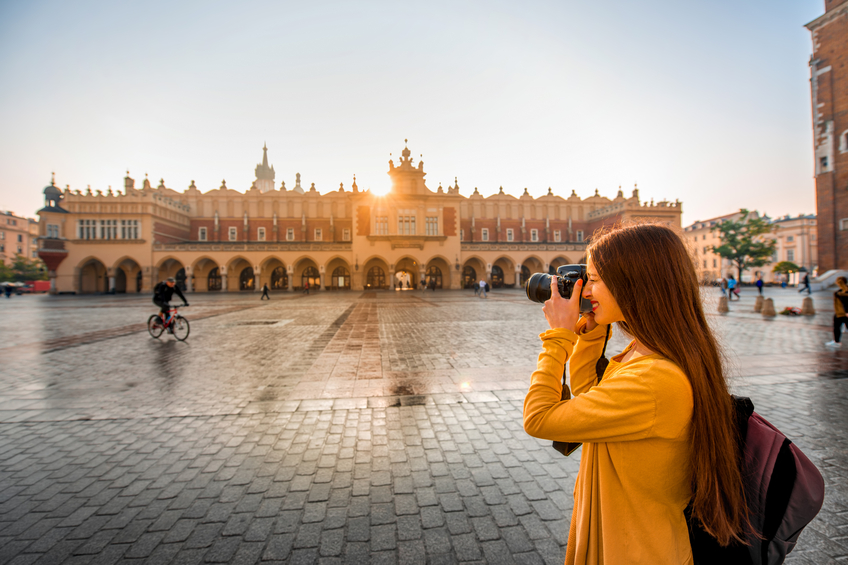Young female tourist with camera and backpack photographing Cloth Hall in the old city center of Krakow