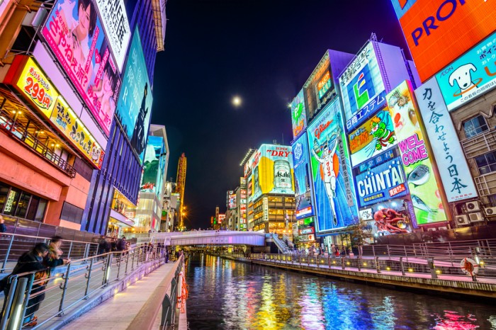 Osaka, Japan - November 25, 2012: Tourists observe the famed advertisements of Dotonbori Canal. With a history dating from 1612, the district is now one of Osaka's primary tourist destinations.