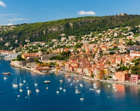 Coast aerial view of scenic French Riviera town Villefranche-sur-Mer with leisure boats anchored in harbor, citadel and fort Mont Alban on hill.