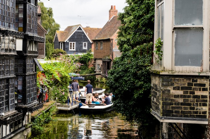 "Canterbury, Kent, England - August 2, 2012. Tourists enjoying a boat ride on the river. The Old Weavers House on the left bank dates from 1500 and is built on the River Stour which is very narrow at this point. The river is flanked on the right by ancient half-timbered houses."