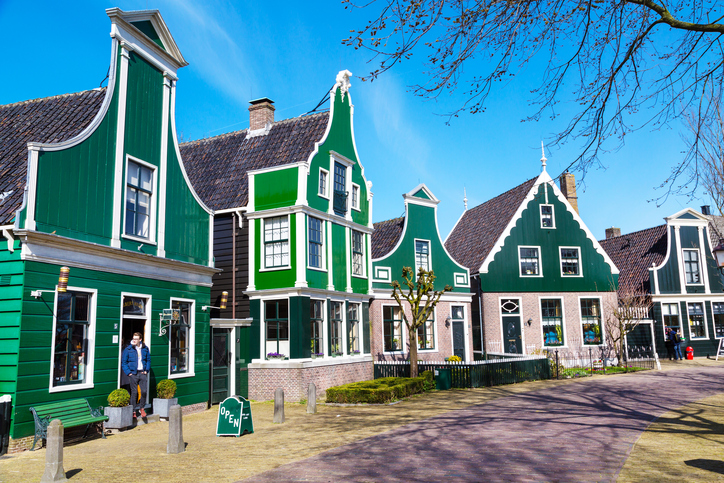 Zaanse schans, Netherlands - April 1, 2016: Zaanse Schans, traditional village, tourists walking, North Holland, green houses against blue cloudy sky