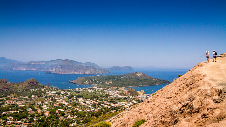 Fossa di Vulcano, Italy - June 12, 2014 - Two hikers enjoy the view over the Aeolian Islands from the volcano crater rim of Fossa di Vulcano on June 12, 2014 in on Vulcano Island, Italy