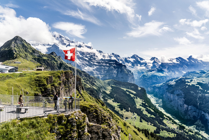 Wengen, Switzerland - August 14, 2019: Swiss alps, Aerial cableway station on top of the Männlichen between Wengen, Lauterbrunnental and Grindelwald. A swiss flag and some tourists on a viewing platform.