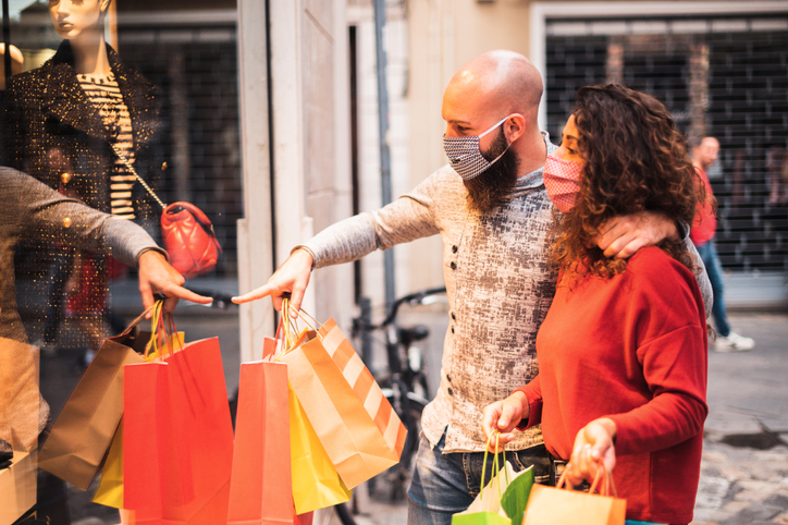 Pretty young man pointing to shop window to show clothing item his likes to his girlfriend - Beautiful young couple enjoying in shopping, having fun together, with the face mask - Consumerism, love, dating, new normal, lifestyle concept