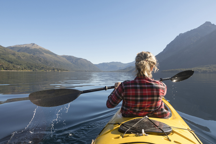 Beautiful woman Enjoying the lakes in her yellow kayak for her summer vacation trip through Patagonia.