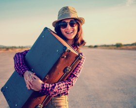 Happy woman traveler embraces a vintage suitcase on road. With a vintage retro instagram filter
