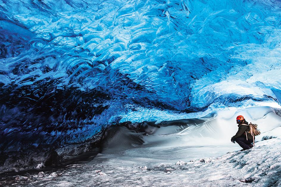 Man traveler enjoying exotic landmark, sitting in the ice cave, Skaftafell glacier, Vatnajokull National park, amazing nature of Iceland