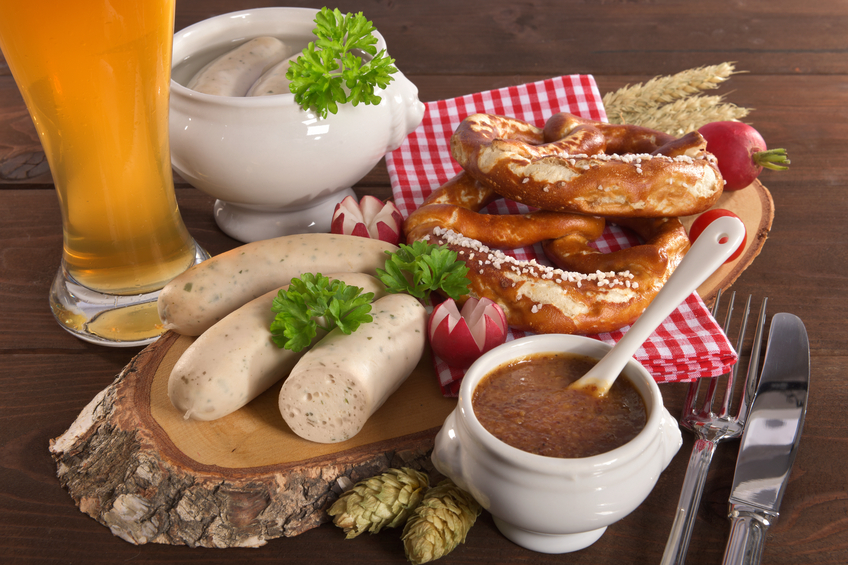 Bavarian veal sausage breakfast with sausages, weissbier, soft pretzel and mild mustard on dark weathered wooden board from Germany