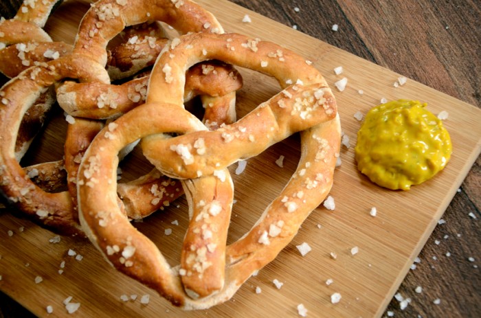 Authentic fresh baked dough pretzel savoury snacks, served on a wooden serving board with mustard, sprinkled with salt