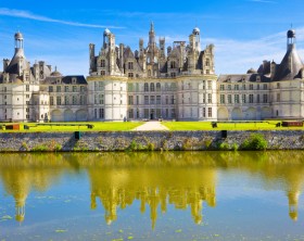 "Chambord, France - July 31, 2009: Great panoramic of Chambord Chateau reflected in the canal in a summer day with blue sky. There are some unrecognizable people in the balconies."