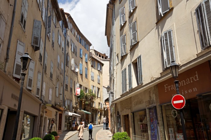 Grasse, France - May 3, 2013: Architecture of Grasse Town in the southern France. It is a city in the French department of Alpes-Maritimes. Grasse is famous for its perfume industry. The city was founded in the XI century. People go along street.