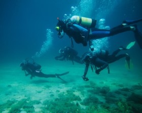 Group of divers underwater with scuba equipment and two of them with action cameras.