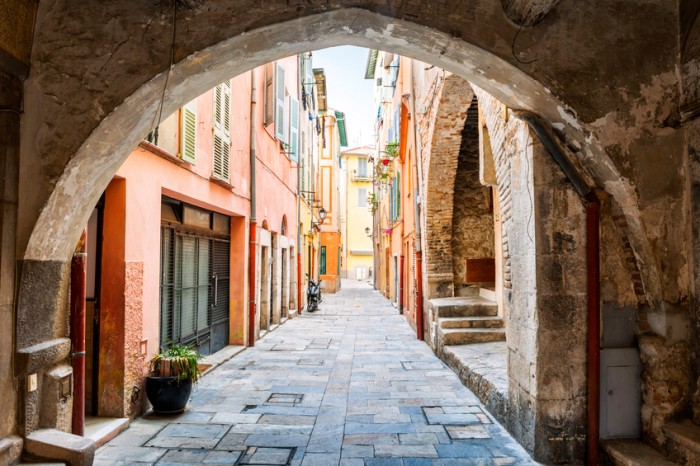 Narrow cobblestone street with colorful buildings viewed though stone arch in medieval town Villefranche-sur-Mer on French Riviera, France.