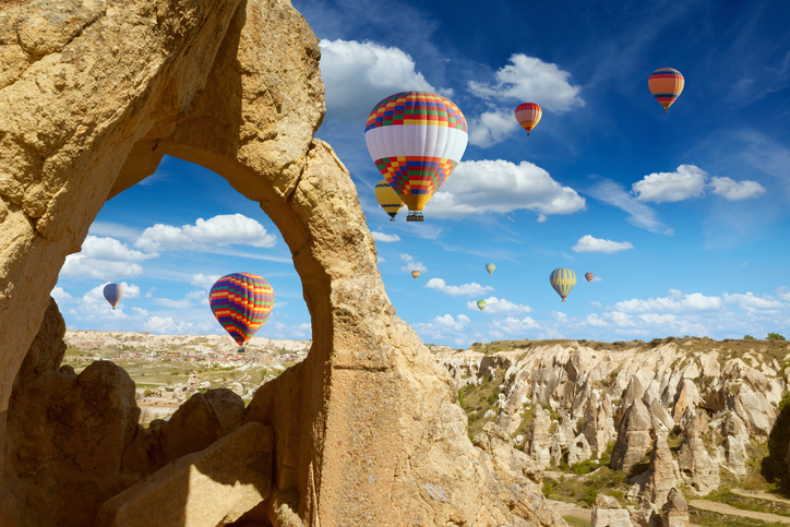 Hand carved arch in limestone rock in Goreme National Park, Cappadocia. Colorful hot air balloons flies in blue sky in Kapadokya, Turkey