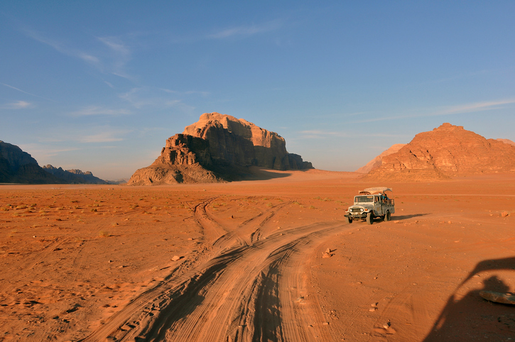 A caravan of jeeps in Wadi Rum Jordan are racing across the desert to get to a special place to see the sunset.