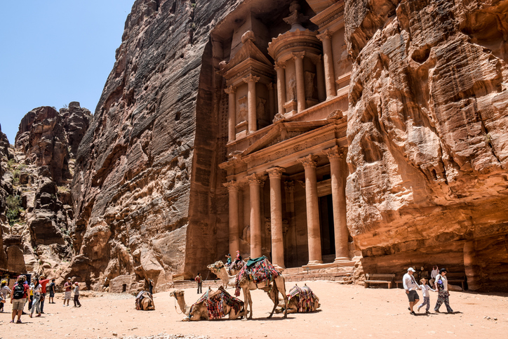 Petra, Jordan - 29 June, 2015: Camels resting in front of the Treasury in Petra Jordan. A family holding hands walking away.