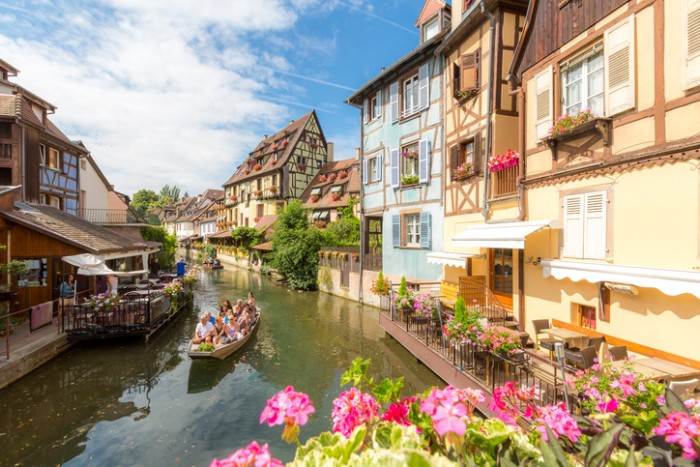 Collar, France- July 13, 2015: Tourist riding boat along canal in Colmar, Petit Venice, Alsace, France. The town is situated along the Alsatian Wine Route and considers itself to be the capital of Alsatian wine.