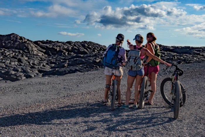 Pahoa, United States - August 3, 2016: Three girls riding the Chain of Craters Road near Kalapana in Volcanoes National Park on the south of Hawaii's Big Island, admire the stunning landscape left behind by the lava from the Kilauea volcano.