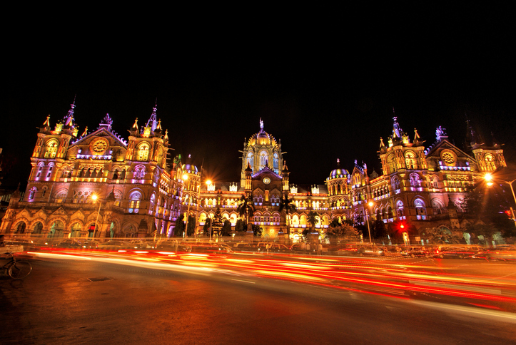Mumbai's CST (Chatrapati Shivaji Terminus) illuminated at night with vehicular traffic in foreground and copy space.