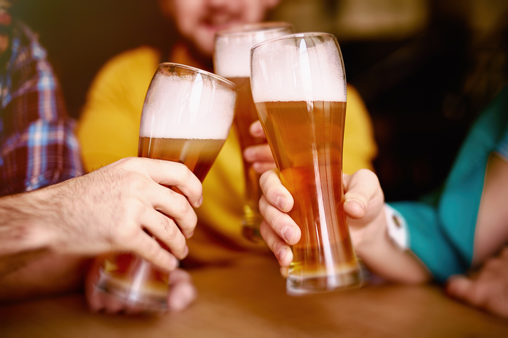 Closeup shot of three elegant tall glasses with delicious craft lager beer and high viscous foam in hands of men meeting round table in Irish Pub
