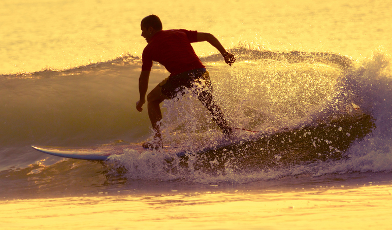 Surfer riding small wave at sunrise