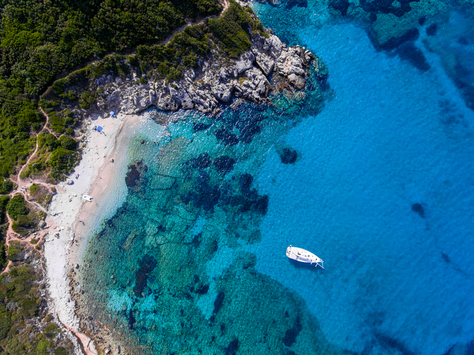 Yacht sailing in the clear blue waters of Porto Timoni, Corfu, Greece, near a beautifull sandy beach.