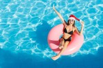 15 hotéis para aproveitar a magia do Natal com a família em 2021 Beautiful happy woman in Santa Claus hat with inflatable ring relaxing in blue swimming pool