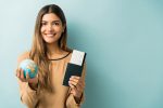 mulher-jovem-feliz-segurando-passaporte-e-cartao-de-embarque-com-globo-em-pe-contra-um-fundo-azul