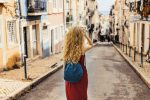 Europa em julho: destinos para aproveitar as férias young-female-red-dress-walking-through-road-surrounded-by-buildings-sunlight